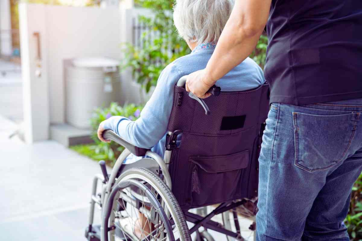 persona che porta anziana su sedia a rotelle