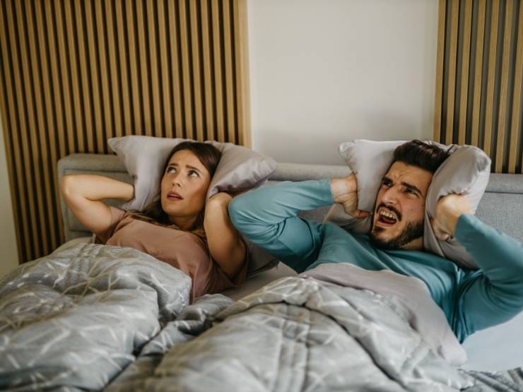 coppia a letto che si tappa le orecchie per i rumori