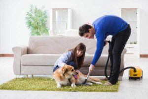 Coppia con cane, lui pulisce tappeto con aspirapolvere