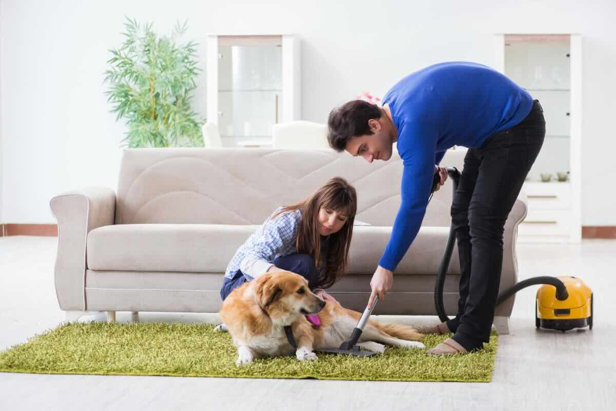 Coppia con cane, lui pulisce tappeto con aspirapolvere