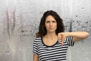 Donna pollice in giù, vetro con goccioline dietro di lei