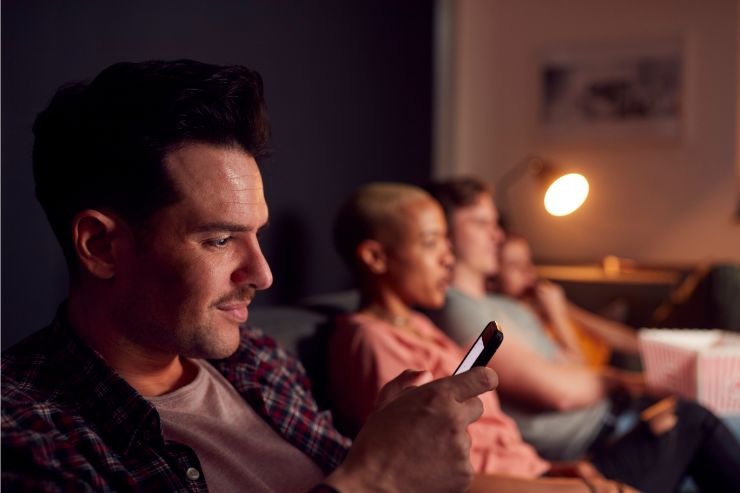 Uomo al cellulare con accanto persone sedute sul divano a guardare TV