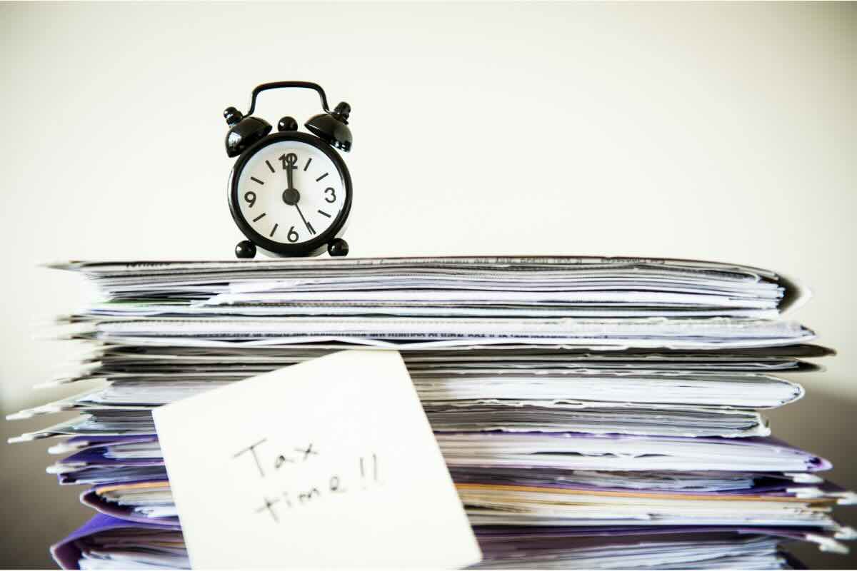 Pila di fogli, sveglia e post it con scritto tax time 
