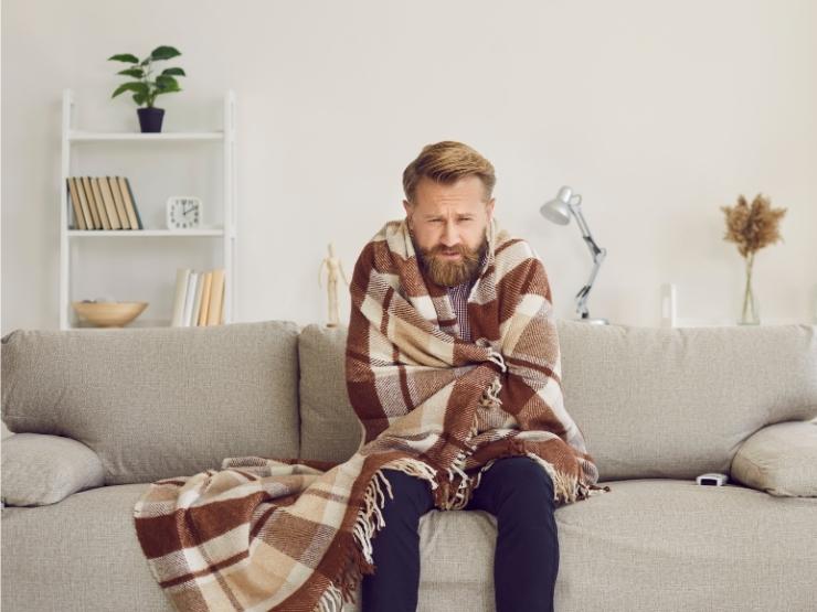 uomo in casa che sente freddo avvolto da coperta