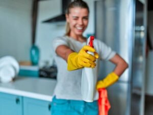 donna sorridente che mostra flacone spray per pulizie